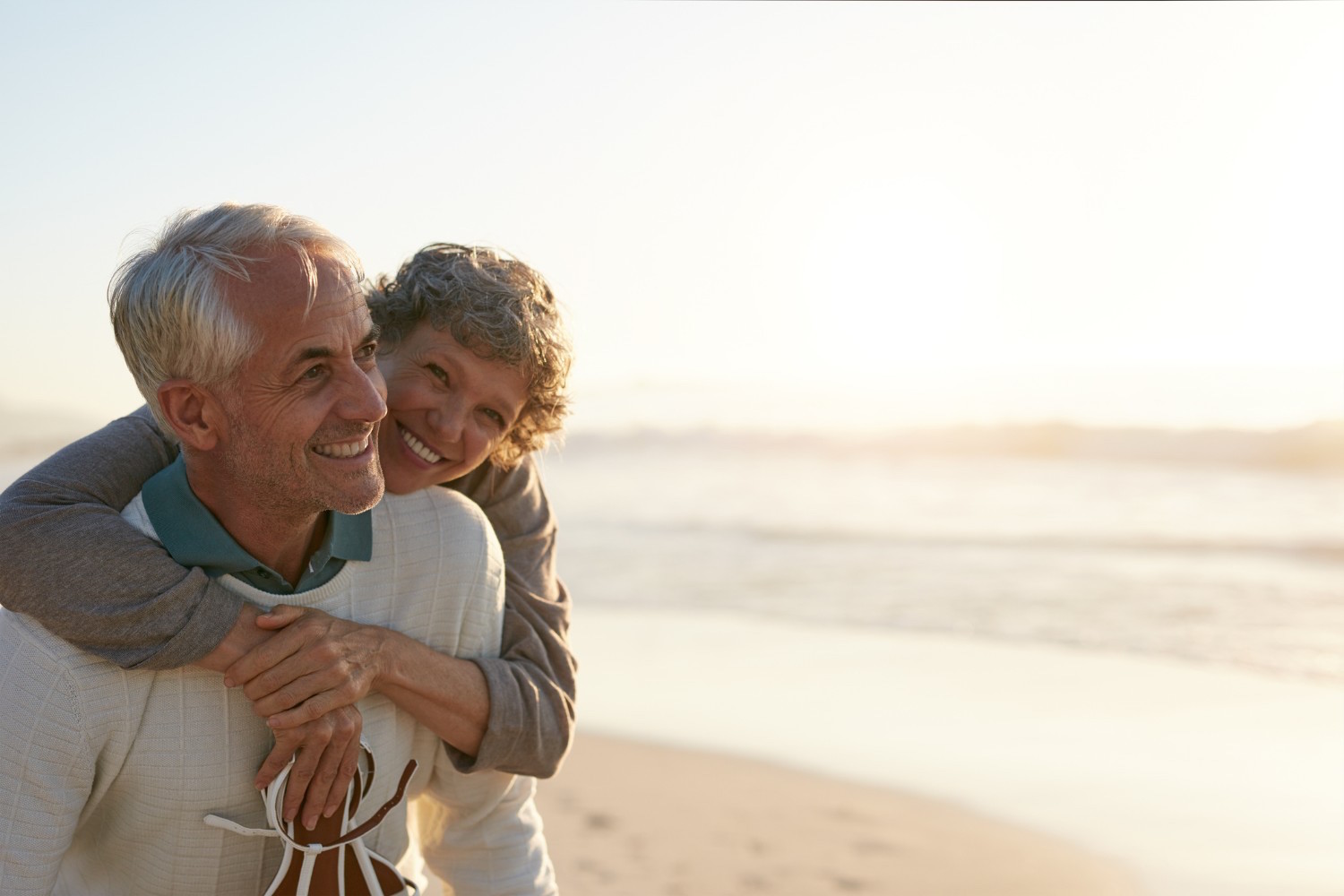 Portrait of happy mature man being embraced by his wife at the beach. Senior couple having fun at the sea shore.