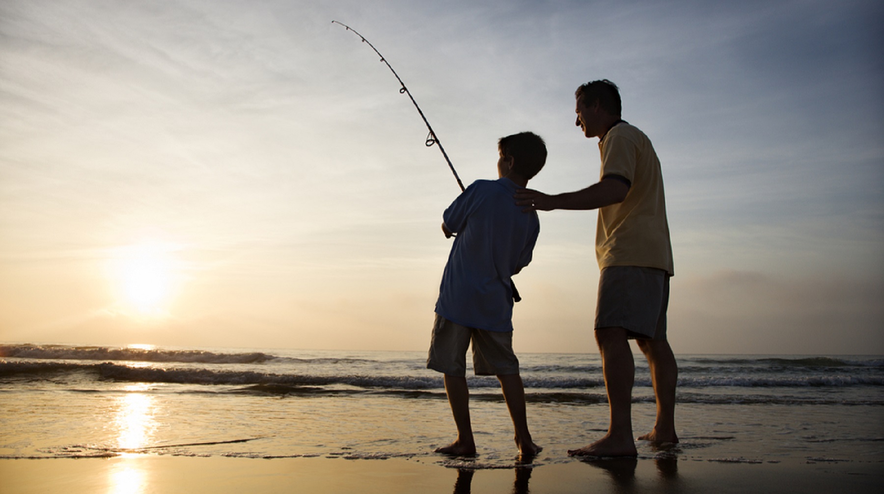 Man and young boy fishing in surf